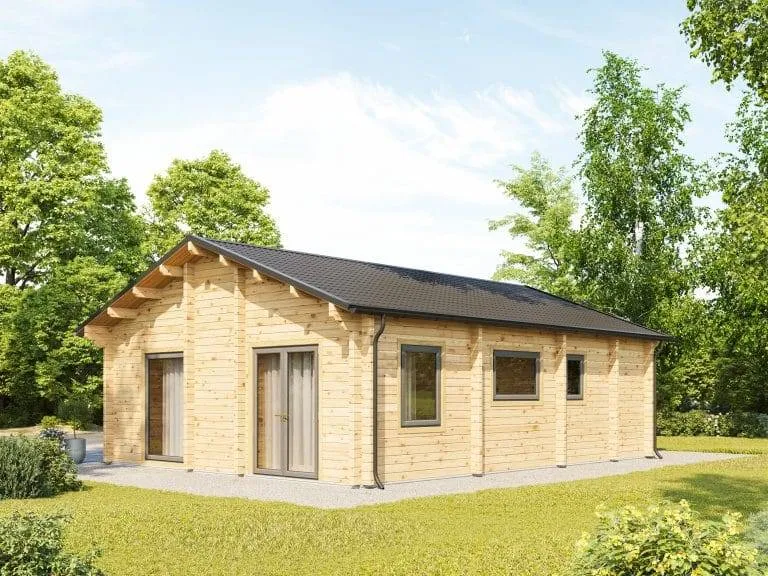 Ein kleines, einstöckiges Holzhaus mit schwarzem Dach steht auf einem Betonfundament. Es hat mehrere Fenster und eine Glastür. Das Haus ist von üppigem Grün und Bäumen unter einem klaren blauen Himmel umgeben.